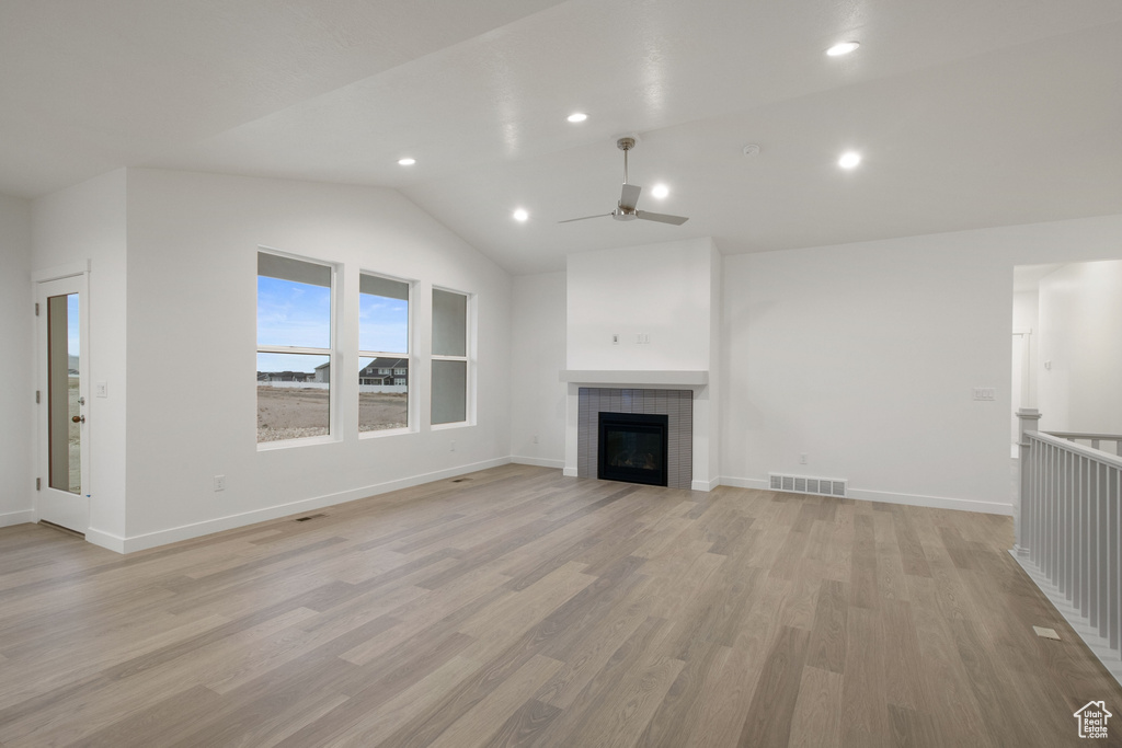 Unfurnished living room featuring light wood-style flooring, a ceiling fan, a tiled fireplace, visible vents, and lofted ceiling