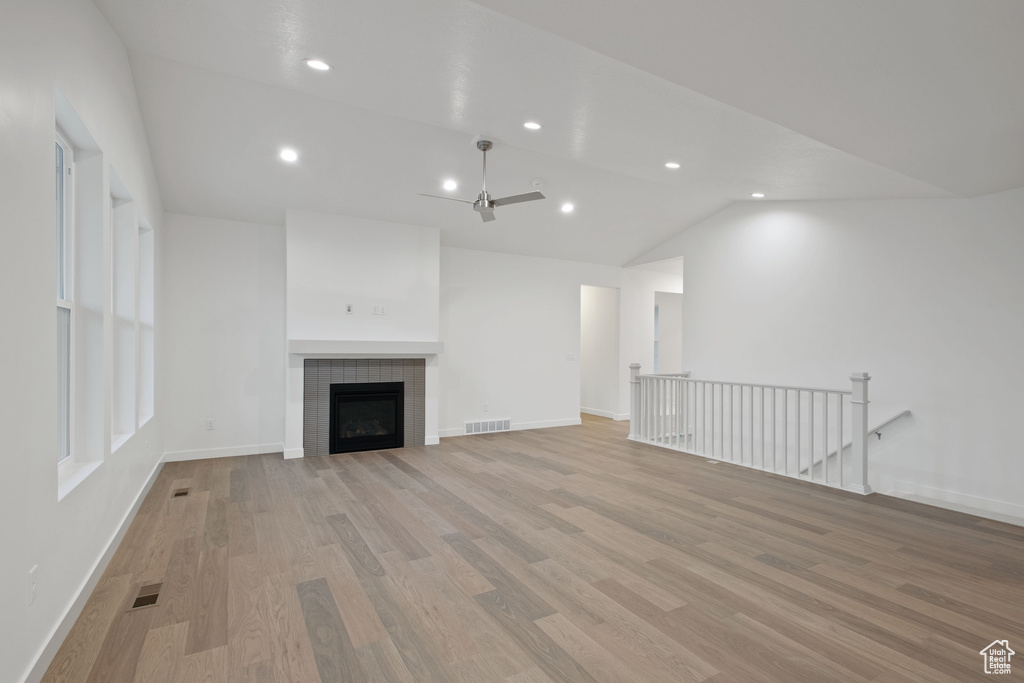 Unfurnished living room with light wood-type flooring, visible vents, recessed lighting, vaulted ceiling, and a tile fireplace