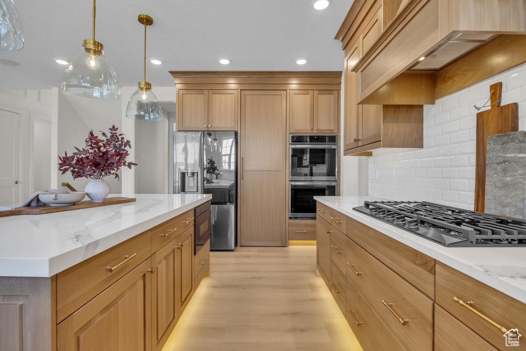 Kitchen featuring light stone countertops, custom range hood, decorative backsplash, black appliances, and light wood-style floors