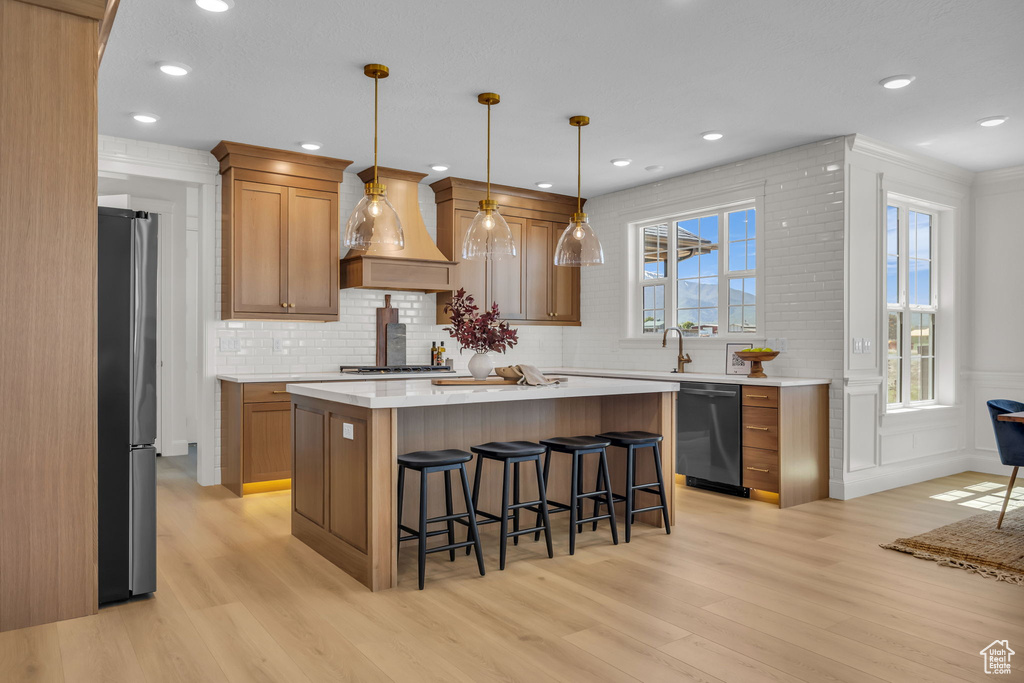 Kitchen featuring stainless steel appliances, light wood finished floors, custom range hood, a kitchen breakfast bar, and light countertops