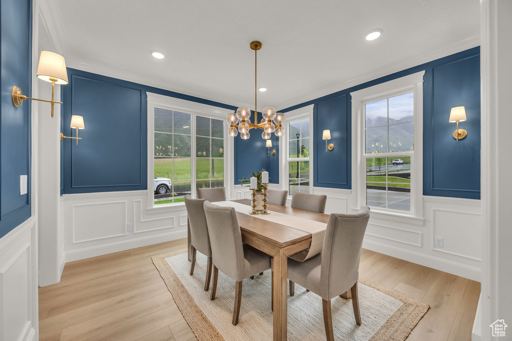 Dining area featuring a decorative wall, crown molding, light wood-style floors, a chandelier, and recessed lighting