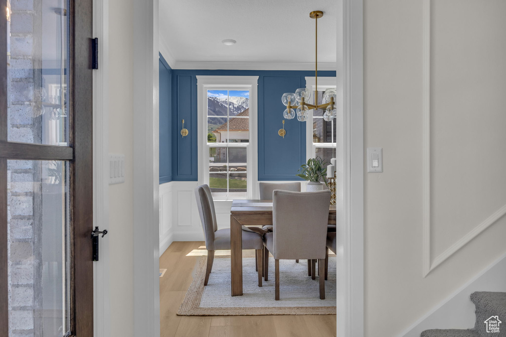 Dining space featuring wood finished floors, a decorative wall, a chandelier, and crown molding