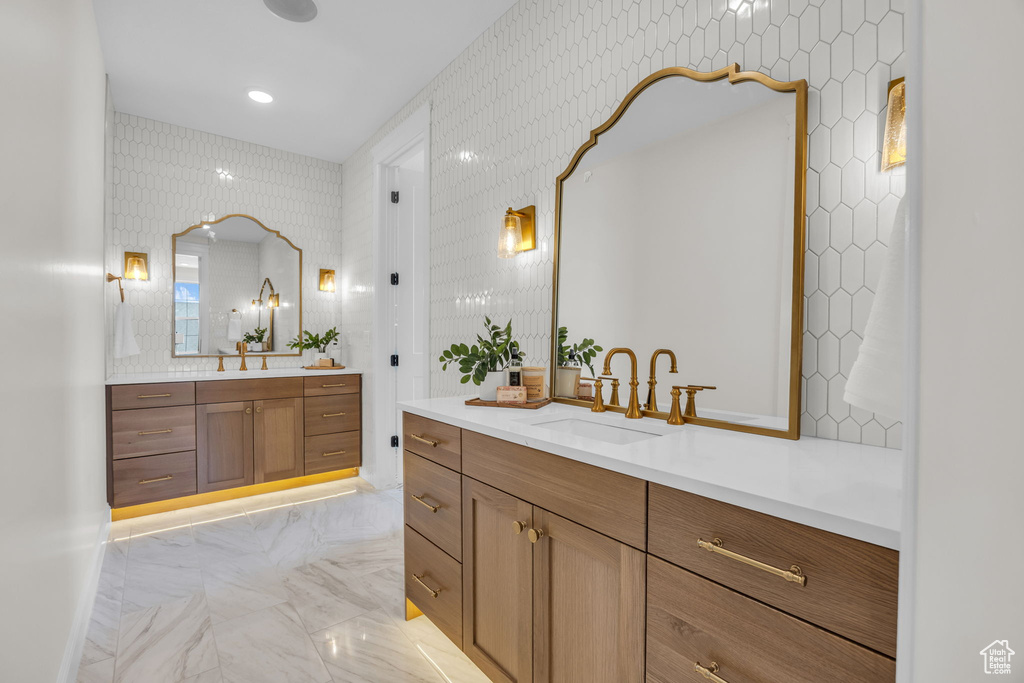 Full bath featuring wallpapered walls, marble finish floor, two vanities, and a sink