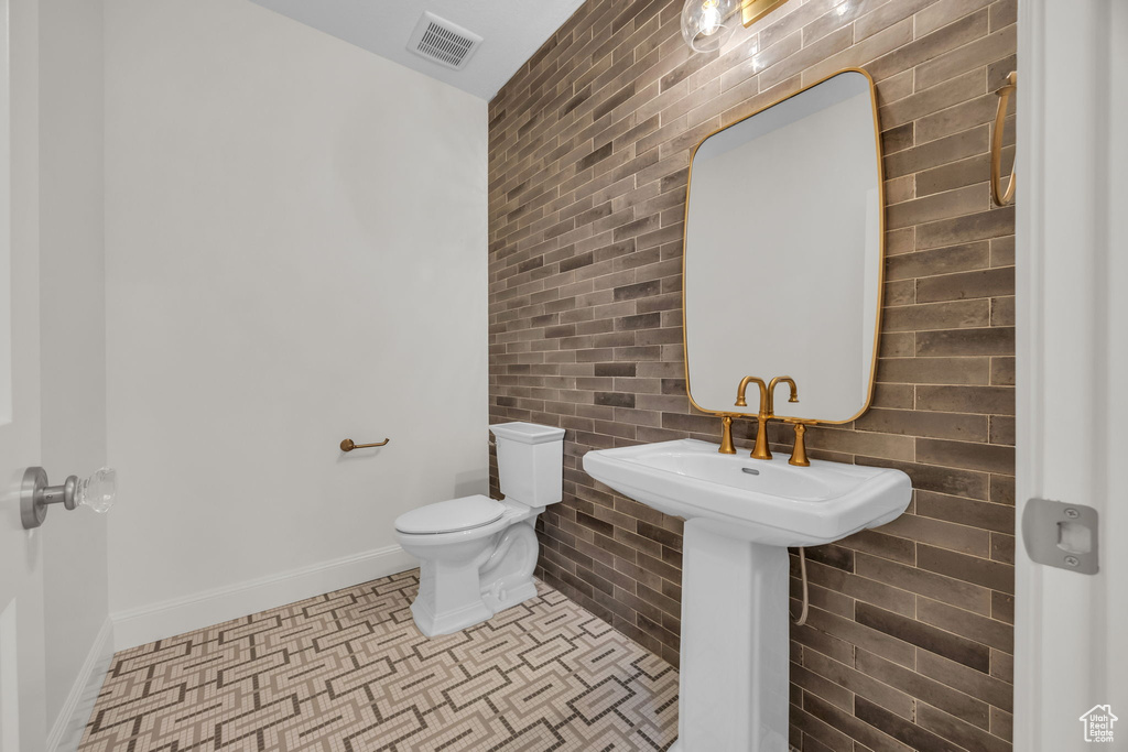 Bathroom with toilet, baseboards, brick wall, and visible vents