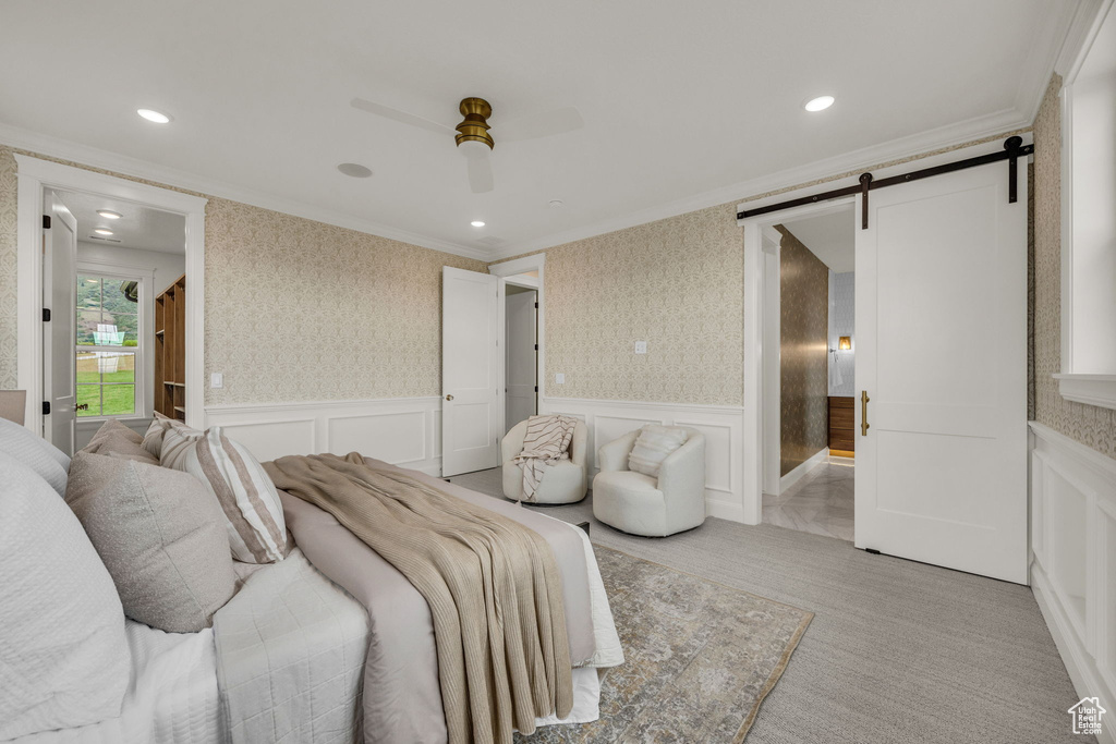 Bedroom with crown molding, a barn door, a decorative wall, a wainscoted wall, and wallpapered walls
