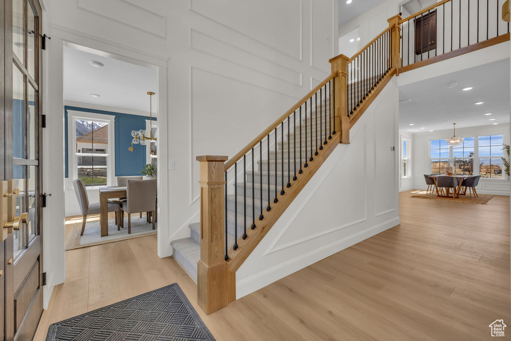 Staircase with a notable chandelier, a healthy amount of sunlight, a decorative wall, and wood finished floors