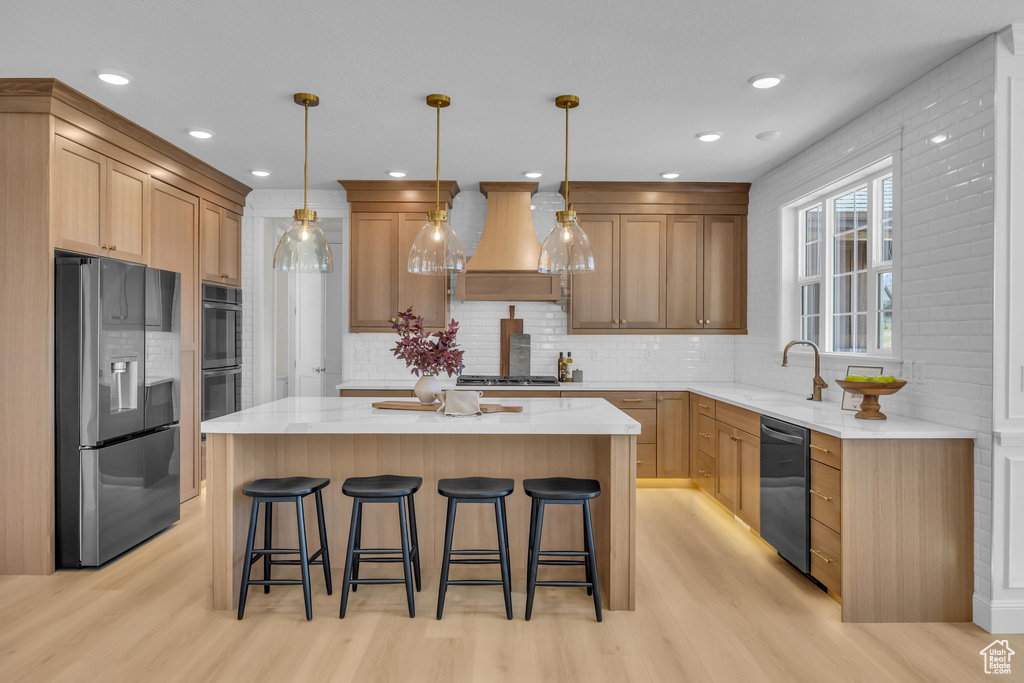Kitchen with a center island, a sink, premium range hood, black appliances, and light wood-type flooring