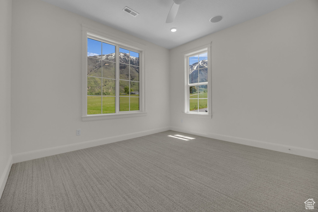 Carpeted empty room with plenty of natural light, visible vents, baseboards, and a ceiling fan