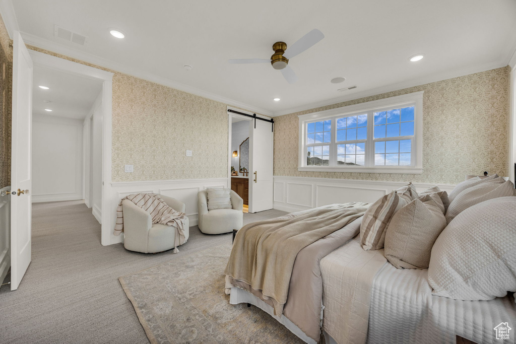 Bedroom featuring ornamental molding, wallpapered walls, a wainscoted wall, a barn door, and carpet flooring