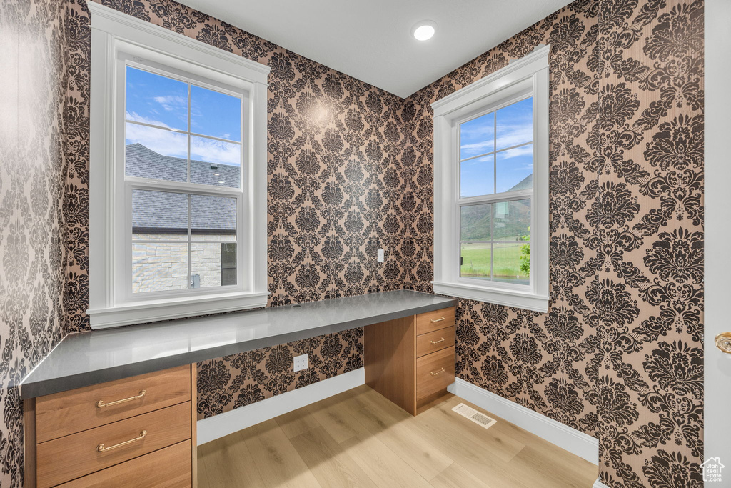 Unfurnished office featuring built in desk, light wood-type flooring, baseboards, and wallpapered walls