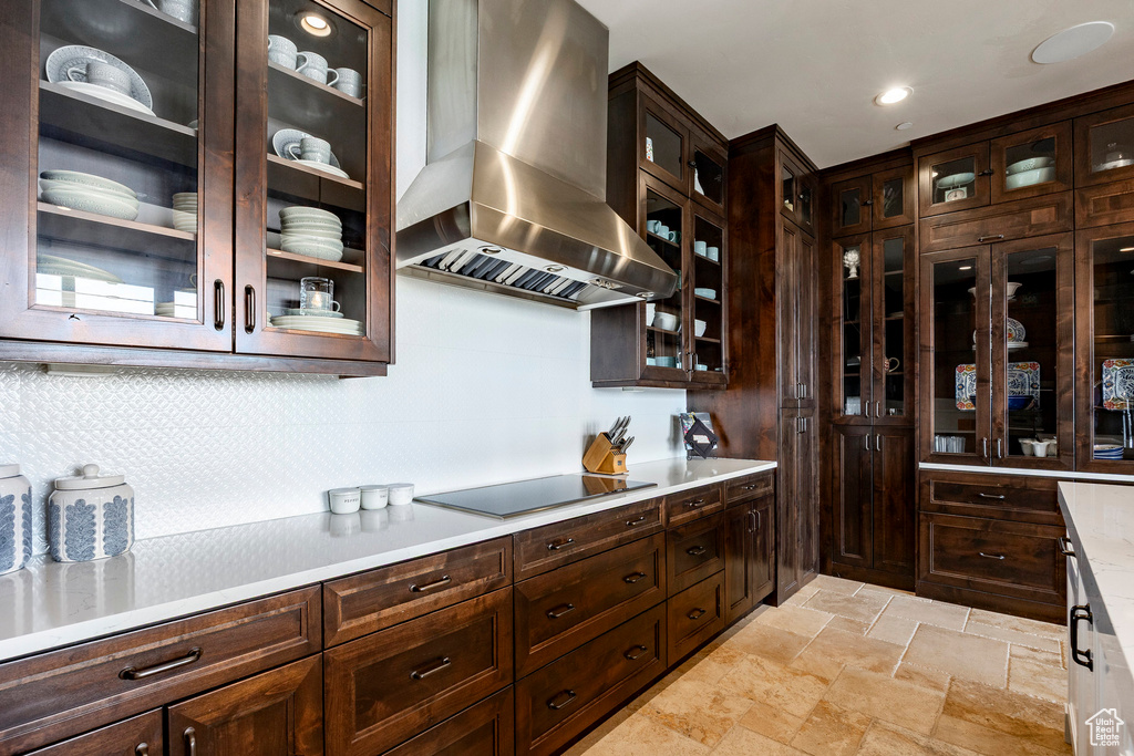 Interior space with ventilation hood, stone tile floors, light countertops, decorative backsplash, and black electric cooktop