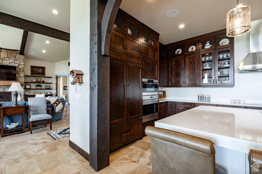 Kitchen featuring glass insert cabinets, dark brown cabinets, stainless steel double oven, open floor plan, and stone tile floors