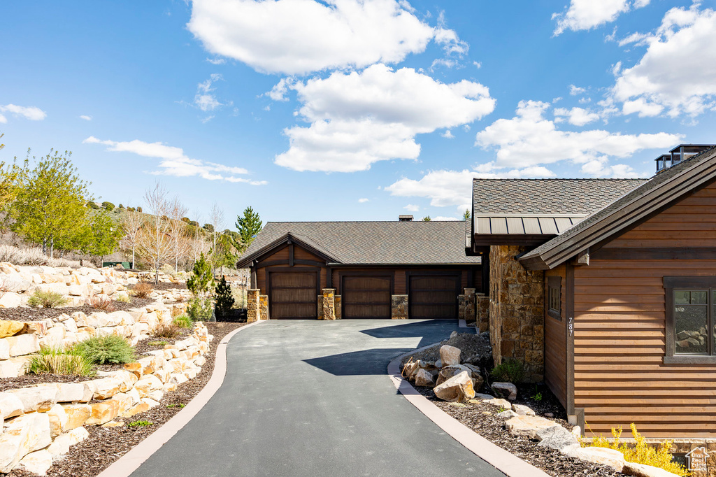 View of front of home with a standing seam roof, aphalt driveway, a garage, stone siding, and roof with shingles
