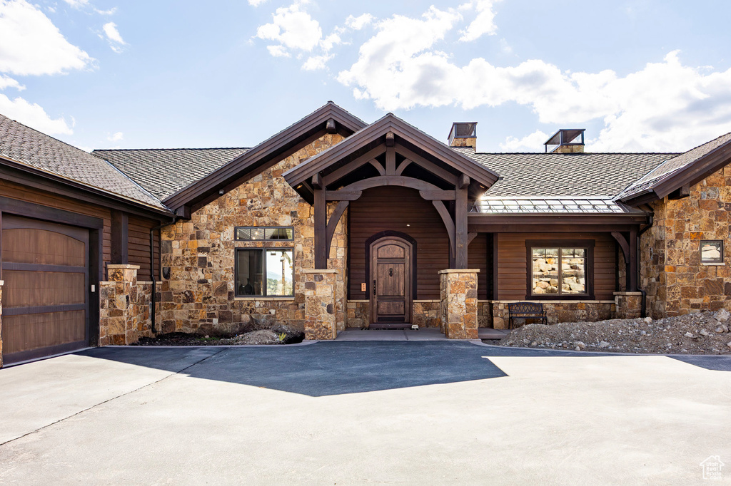 Entrance to property featuring a chimney, driveway, a standing seam roof, metal roof, and stone siding