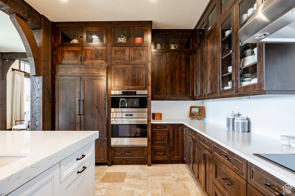 Kitchen with paneled built in refrigerator, stainless steel double oven, stone finish floor, white cabinetry, and arched walkways