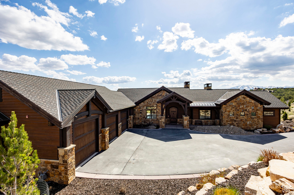 Chalet / cabin with a chimney, driveway, an attached garage, a shingled roof, and stone siding
