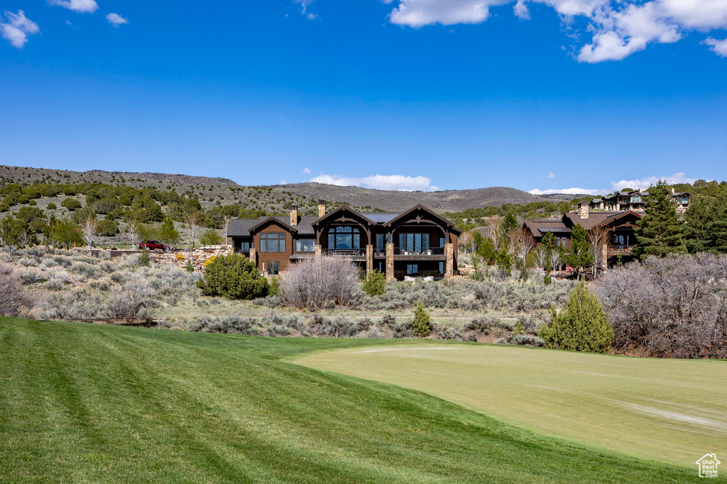 Rear view of house featuring a mountain view, a chimney, golf course view, and a lawn