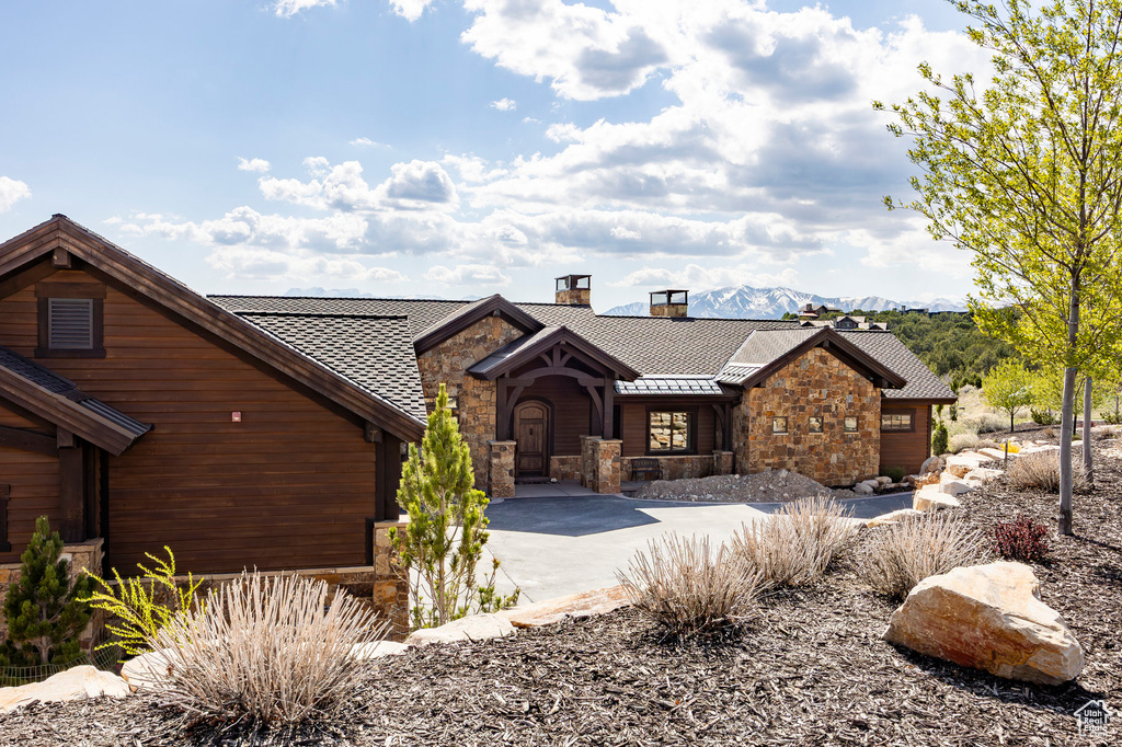 Chalet / cabin featuring stone siding, a mountain view, a chimney, and concrete driveway