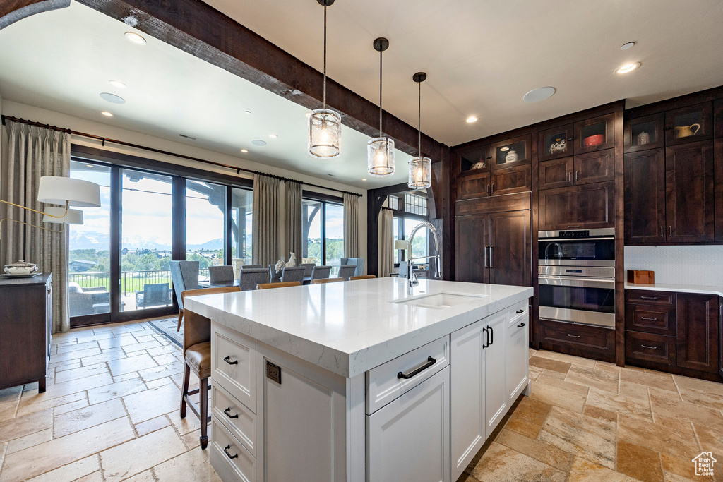 Kitchen with white cabinetry, double oven, stone tile floors, and a sink
