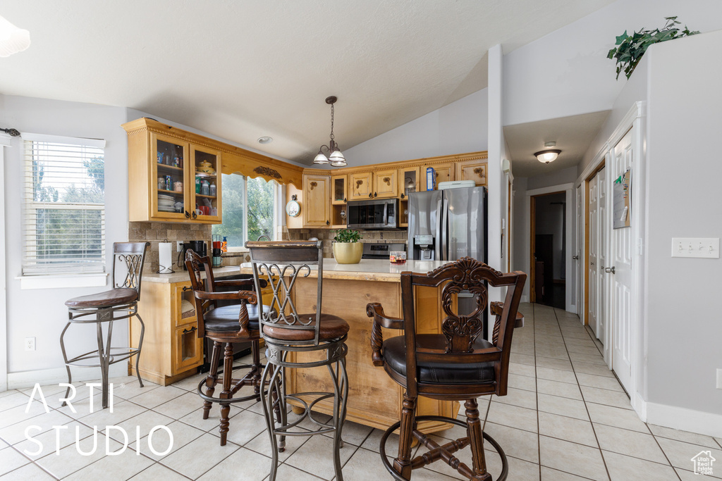 Kitchen featuring stainless steel appliances, light tile patterned floors, vaulted ceiling, light countertops, and tasteful backsplash