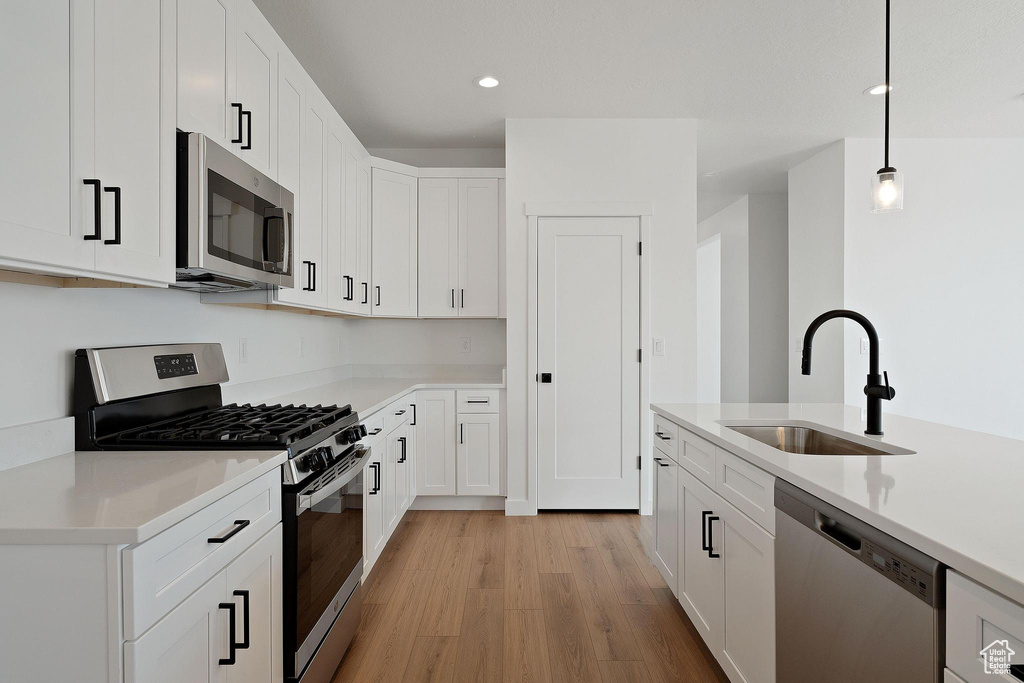 Kitchen featuring a sink, light wood finished floors, light countertops, white cabinets, and appliances with stainless steel finishes