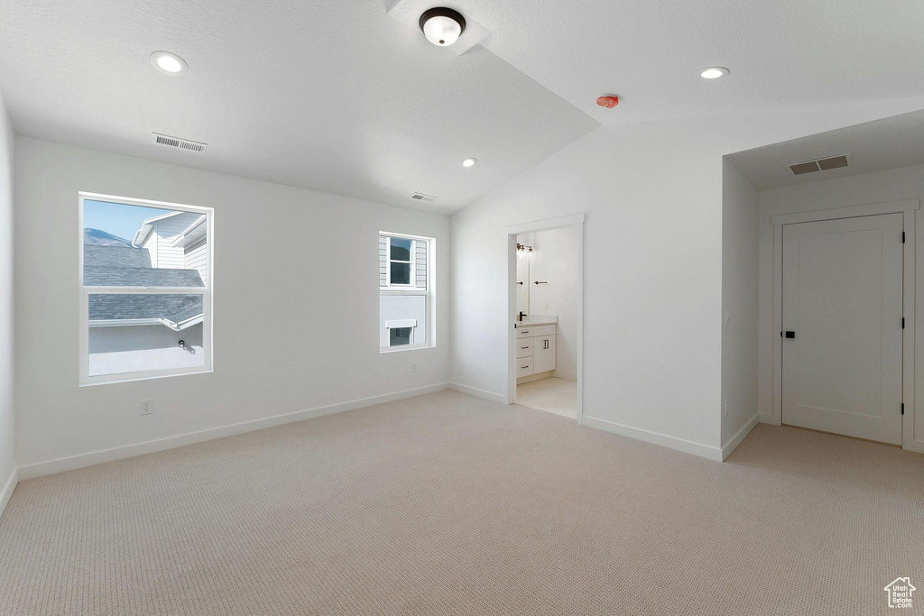 Unfurnished bedroom featuring light colored carpet, visible vents, baseboards, and vaulted ceiling