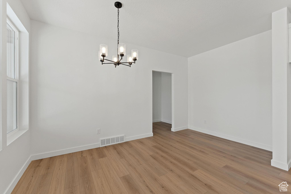 Unfurnished dining area with light wood-style floors, visible vents, baseboards, and a notable chandelier