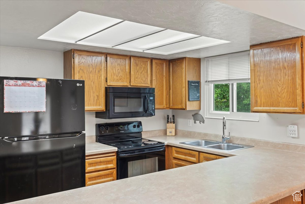 Kitchen featuring black appliances, light countertops, a sink, and brown cabinets