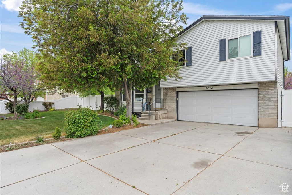 View of front of house featuring an attached garage, fence, a front lawn, brick siding, and driveway