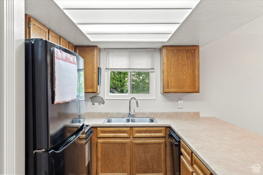 Kitchen with a sink, brown cabinetry, light countertops, and black appliances