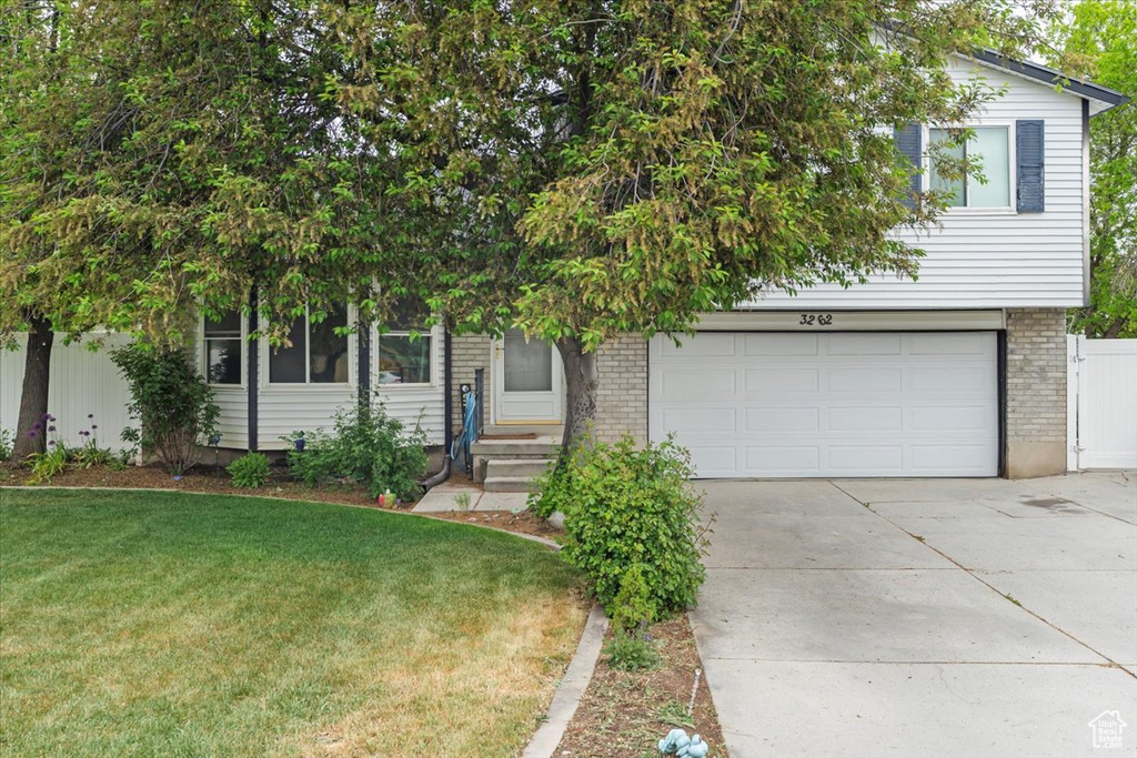 Obstructed view of property featuring concrete driveway, a garage, brick siding, and a front yard