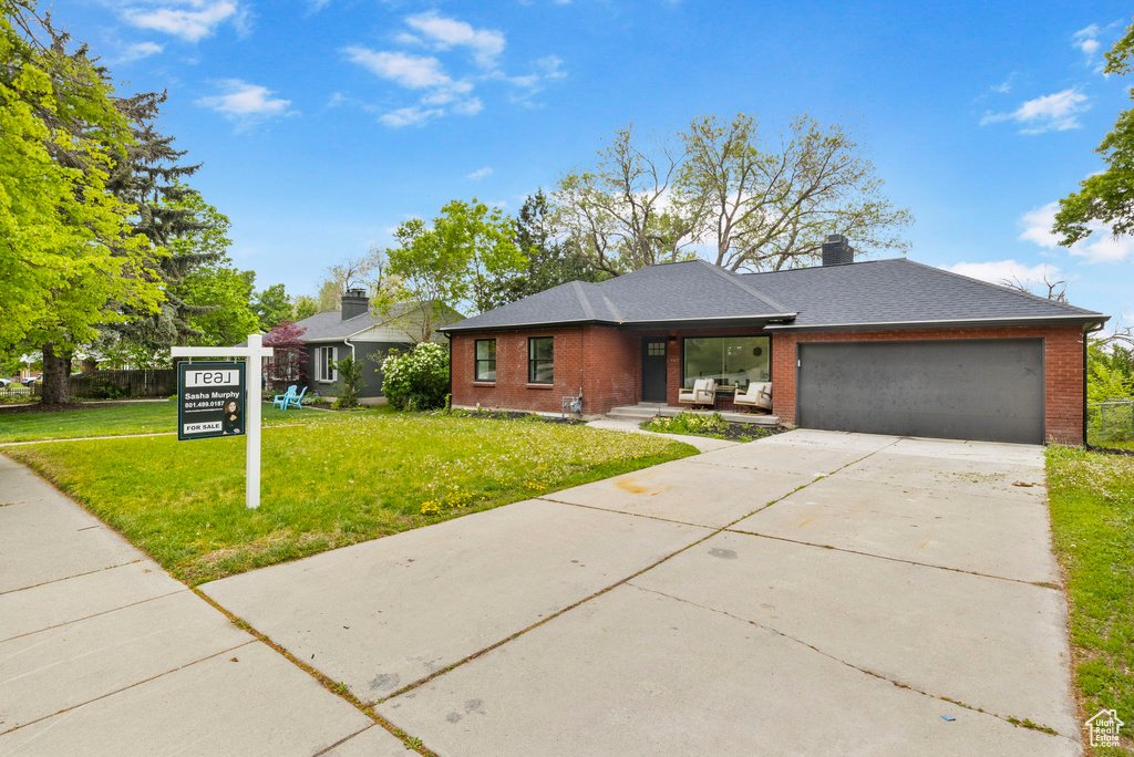 View of front of home with a chimney, brick siding, a garage, concrete driveway, and a front yard