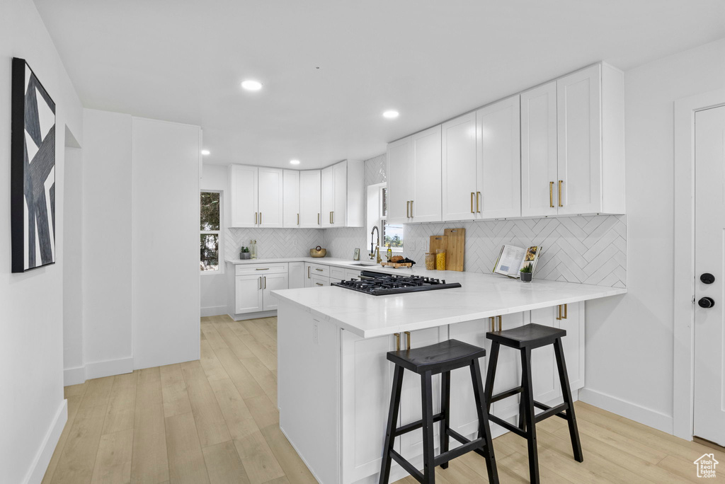 Kitchen with black gas cooktop, light wood finished floors, backsplash, and light countertops