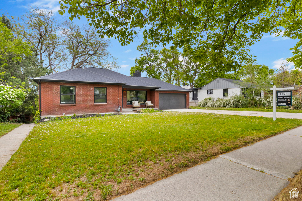 Ranch-style house featuring concrete driveway, a garage, brick siding, and a front yard