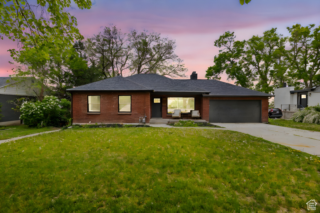 Single story home with brick siding, driveway, a garage, a chimney, and a lawn