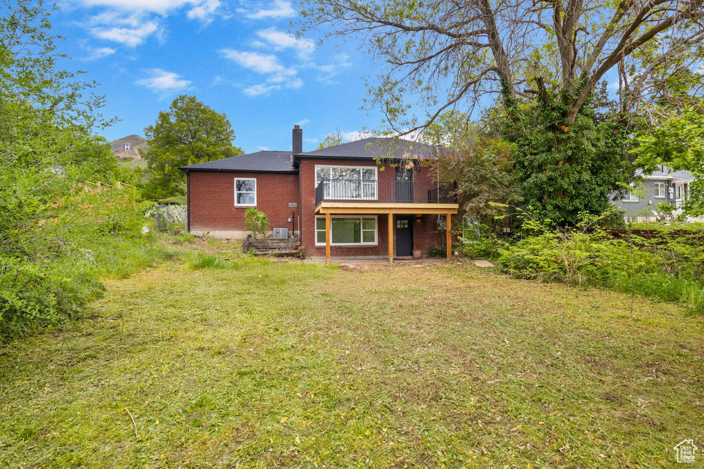 Rear view of house with a chimney, a wooden deck, brick siding, and a lawn
