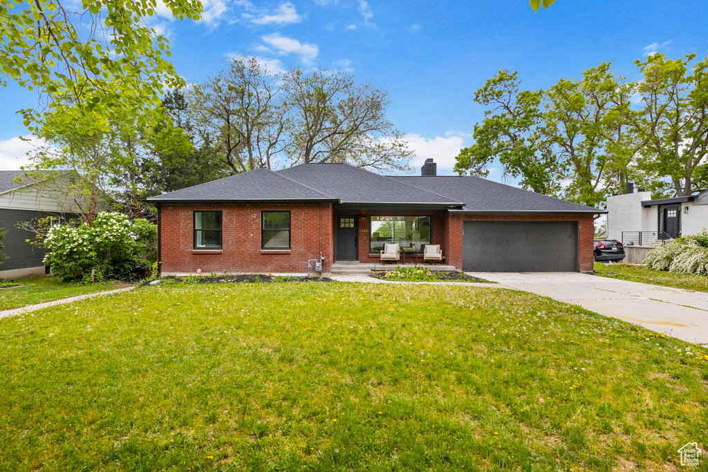View of front of home with brick siding, covered porch, a garage, concrete driveway, and a front yard