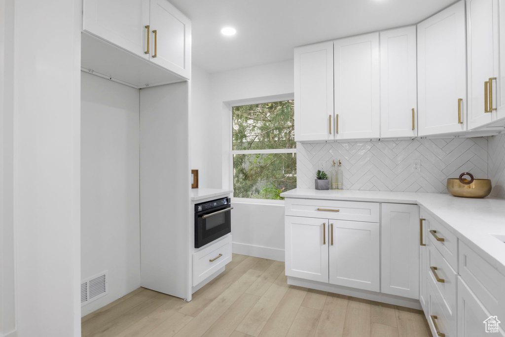 Kitchen with visible vents, black oven, backsplash, light wood-style floors, and light countertops