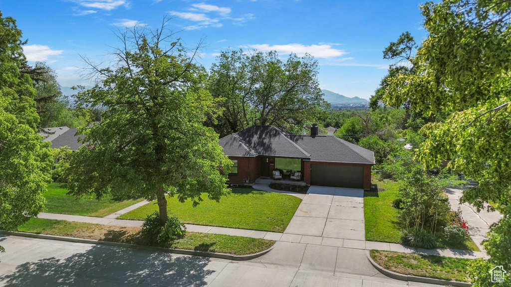 View of front of property featuring an attached garage, a front yard, concrete driveway, roof with shingles, and a mountain view