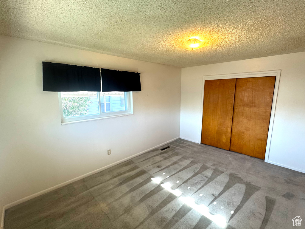 Unfurnished bedroom with a textured ceiling, carpet, a closet, and visible vents