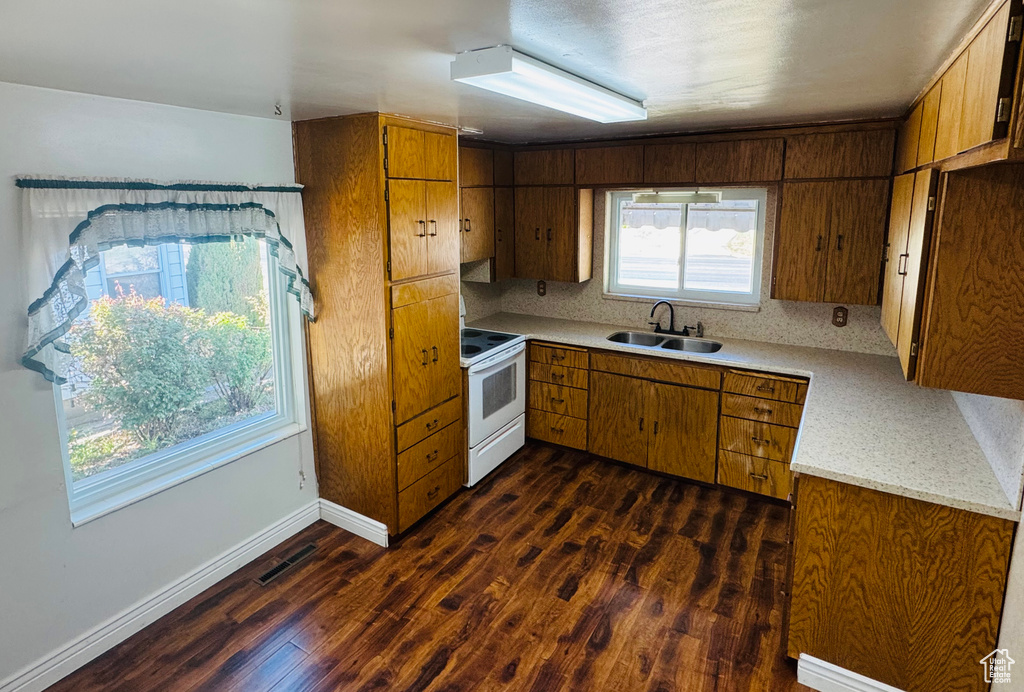 Kitchen featuring a sink, brown cabinets, dark wood-type flooring, light countertops, and electric stove