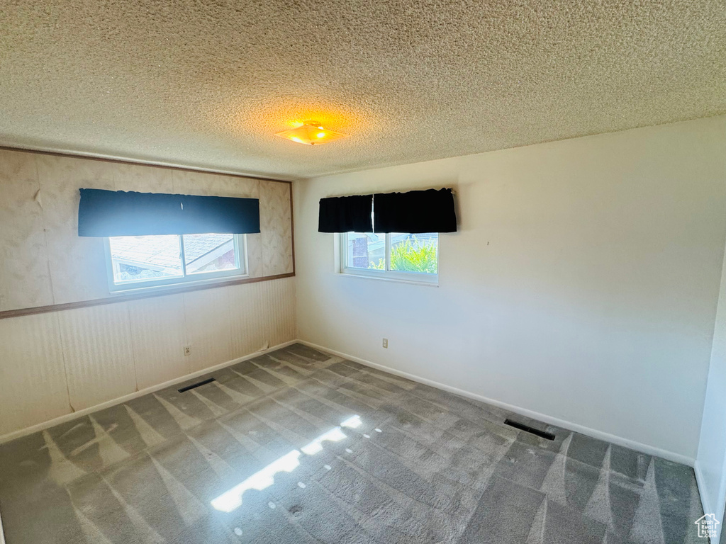 Empty room featuring a textured ceiling, visible vents, and carpet