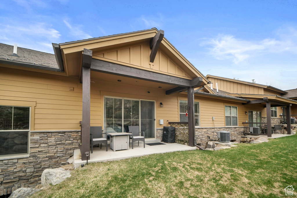 Back of property featuring stone siding, board and batten siding, a patio area, and a lawn