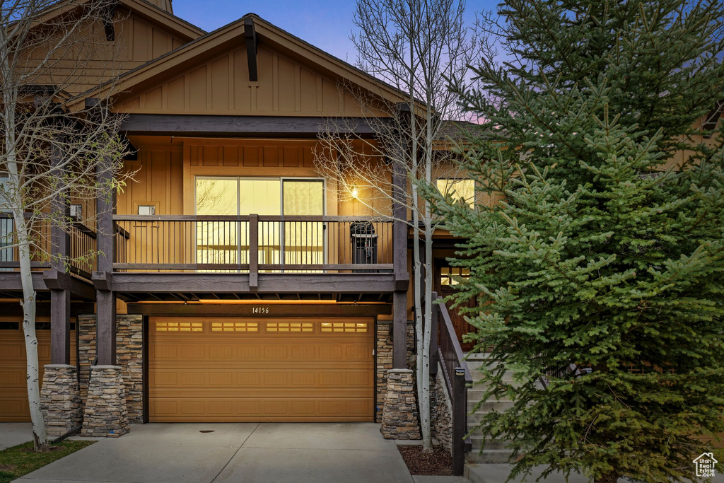 Craftsman house featuring a balcony, board and batten siding, driveway, an attached garage, and stone siding