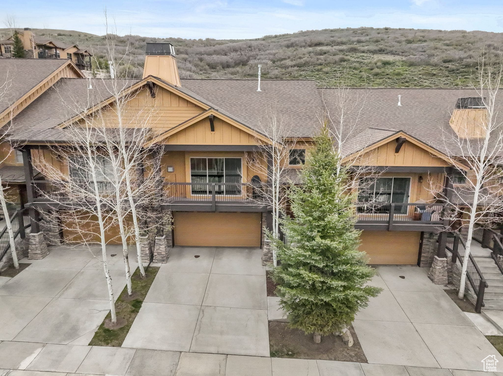 Craftsman inspired home featuring a chimney, driveway, a balcony, a garage, and a shingled roof