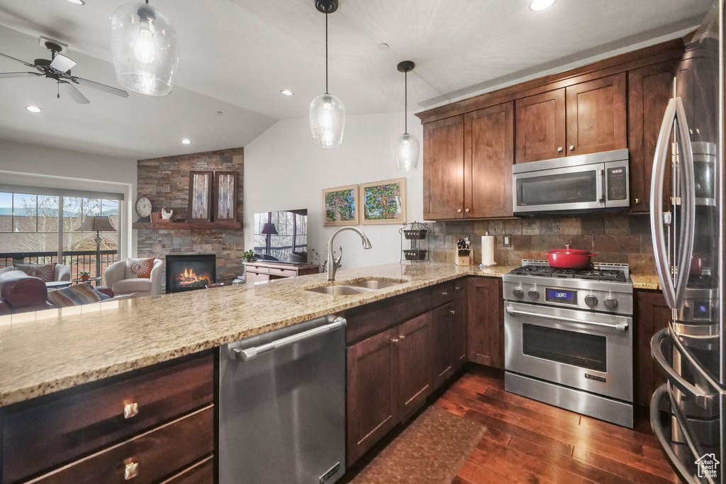 Kitchen featuring vaulted ceiling, a stone fireplace, a sink, dark wood-type flooring, and stainless steel appliances