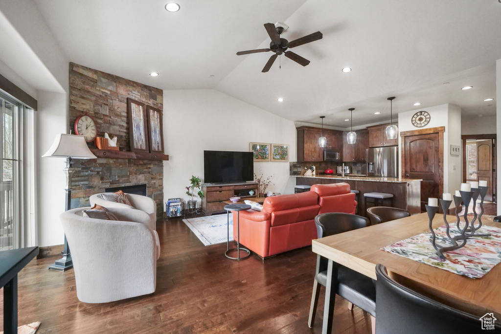 Living area with dark wood-style flooring, a stone fireplace, ceiling fan, vaulted ceiling, and recessed lighting