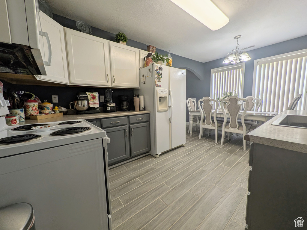Kitchen with pendant lighting, white appliances, light wood finished floors, an inviting chandelier, and light countertops