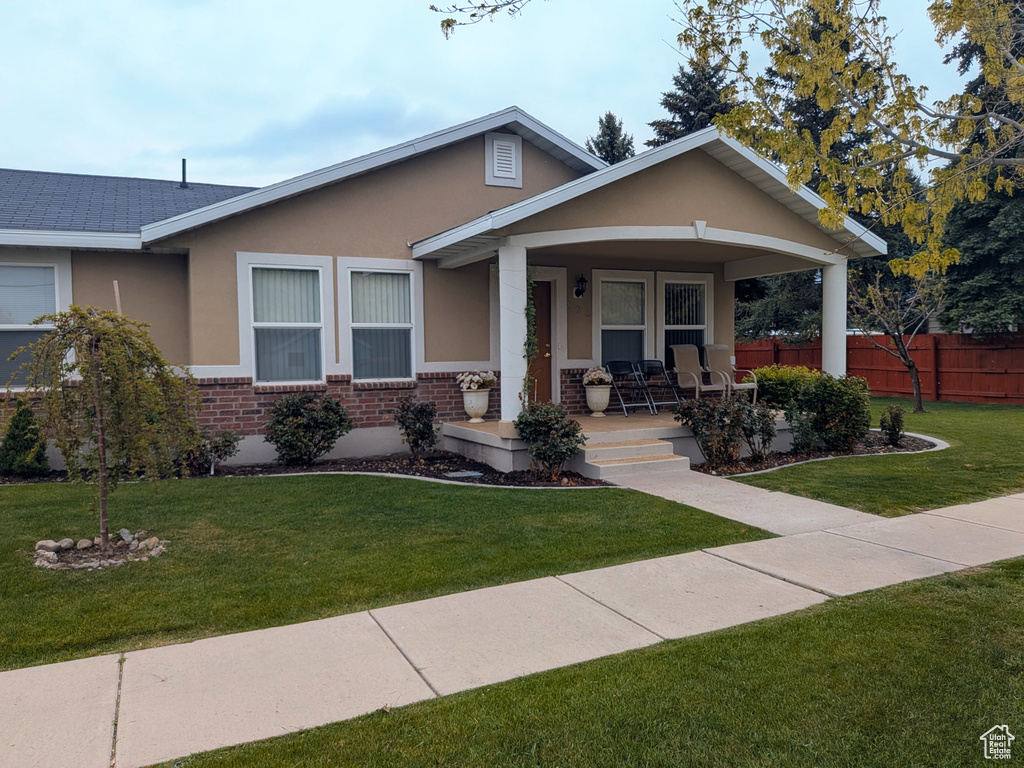 View of front of home featuring stucco siding, fence, a front lawn, a porch, and brick siding