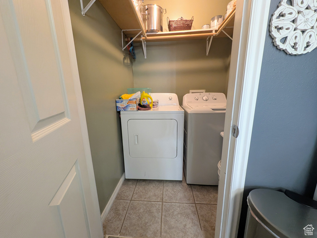 Clothes washing area with washing machine and dryer, baseboards, light tile patterned flooring, and laundry area